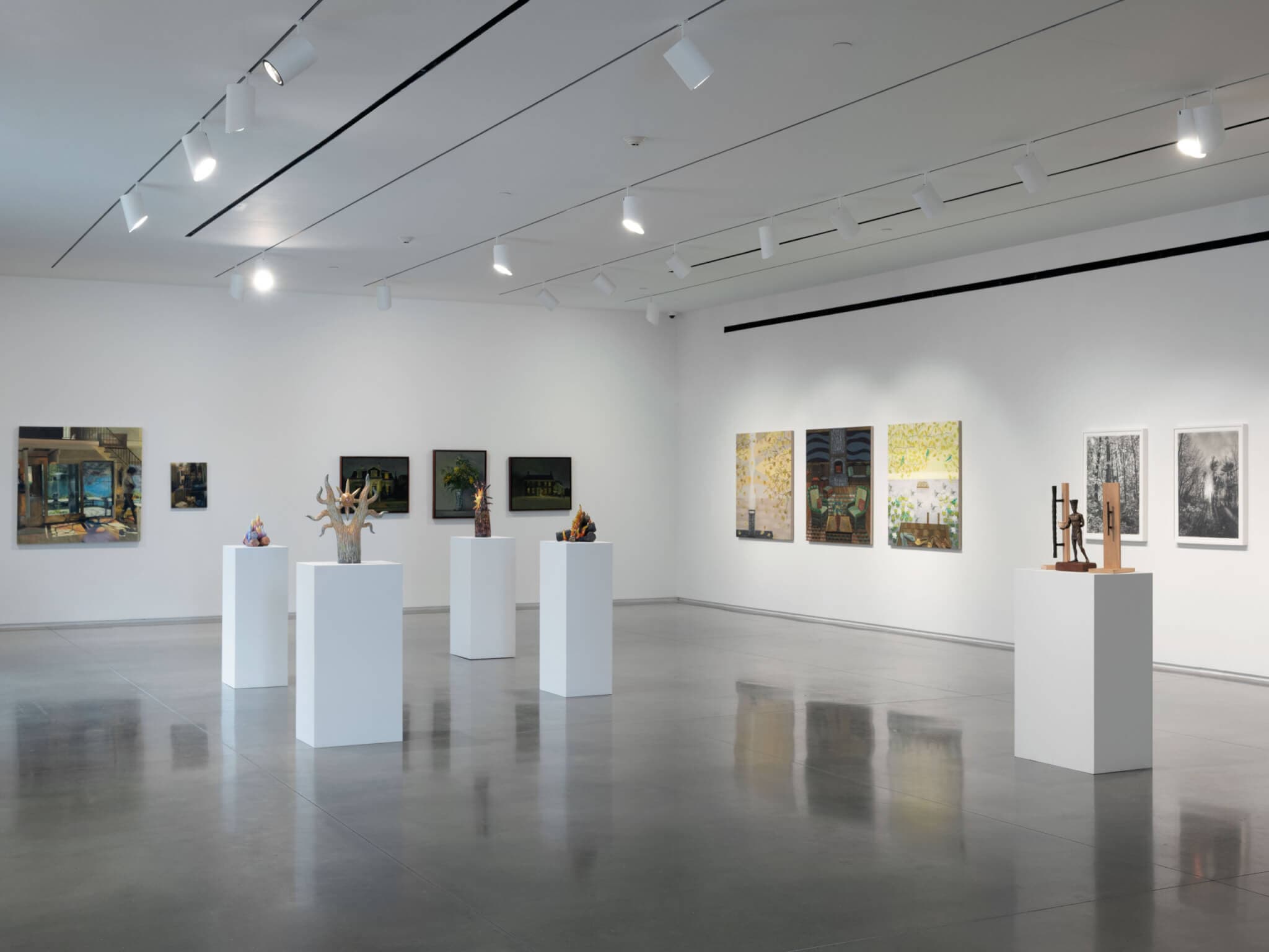 Ten painted artworks line a gallery's walls while five white pedestals showcase small sculptures.